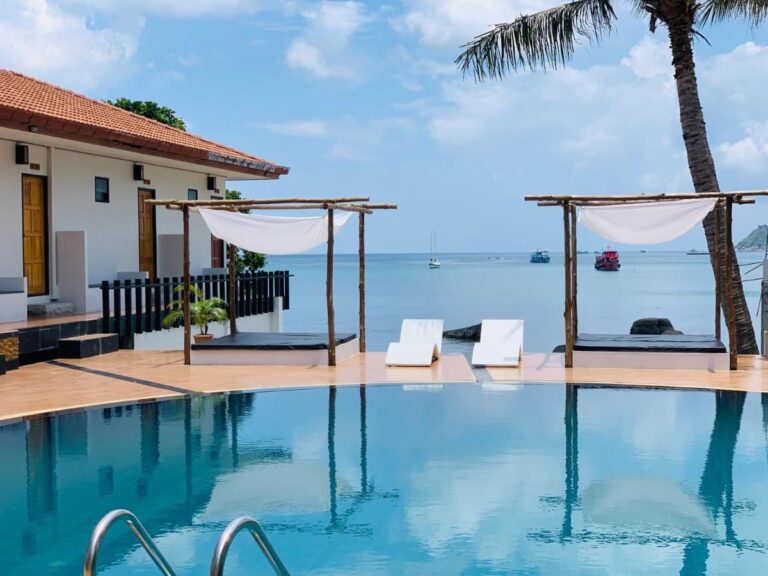 La piscina frente al mar, con dos camas bajo una pérgola y tumbonas blancas