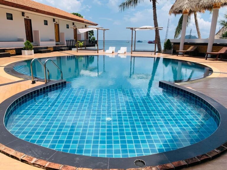 La piscina de azulejos azules, con el mar y barcos al fondo