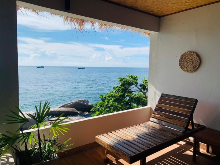 Una terraza cubierta con una tumbona de madera, frente al mar y a las rocas