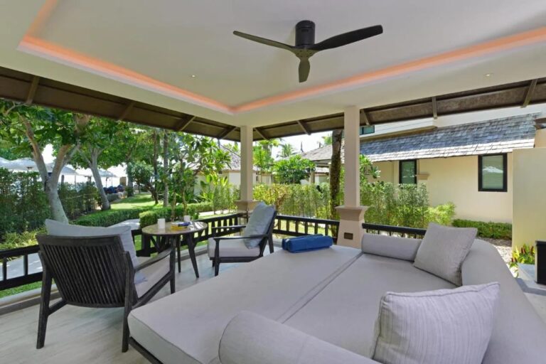 Una terraza cubierta con una gran cama de descanso, dos sillones y un ventilador de techo