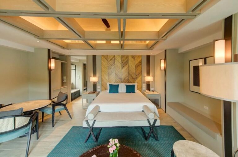 Una habitación con cama grande delante de un panel de madera en espiga, con un banco y una alfombra verde azulada