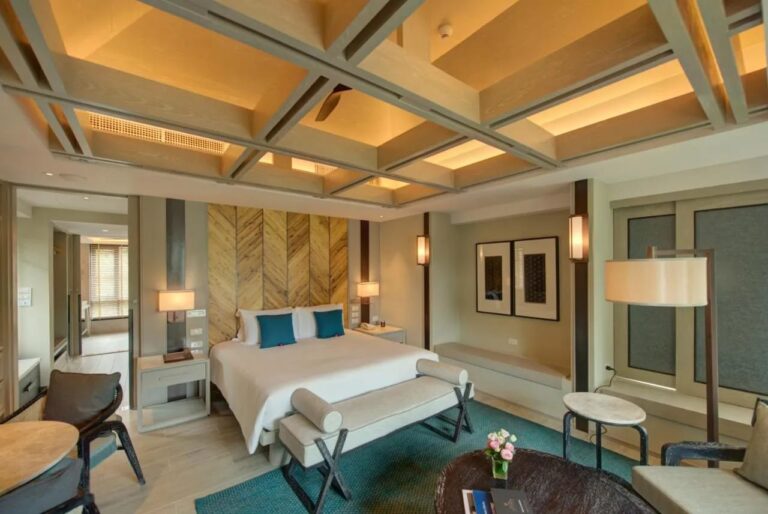 Una habitación con cama grande, una lámpara de pie y un banco bajo la ventana