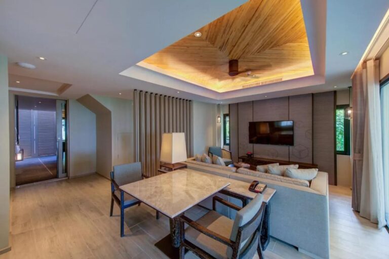 Una sala de estar con mesa de mármol, un sofá grande y un televisor en la pared