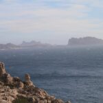 Desde las rocas calizas del Frioul en primer plano, vista de un mar agitado y cubierto de espuma hasta la isla Maïre y la costa de Les Goudes, recortadas en la bruma.