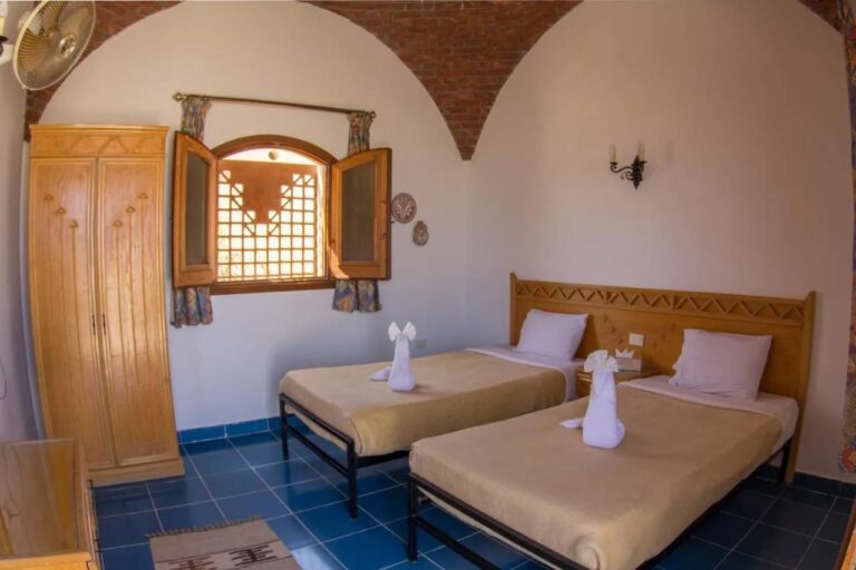 Una habitación con dos camas bajo una bóveda de ladrillo, con un armario y contraventanas de madera