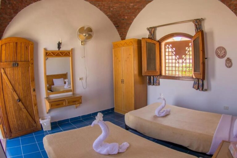 Una habitación con dos camas, una puerta de madera, un espejo y un armario