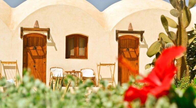 Las fachadas abovedadas de los chalets, con sus puertas de madera y un hibisco rojo en primer plano