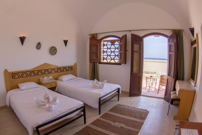Una habitación con dos camas abierta a una terraza, frente a la playa y al mar