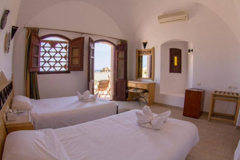 Una habitación con dos camas bajo una bóveda blanca, con la puerta abierta a una terraza y al mar