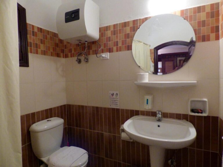 Un baño con lavabo, inodoro, espejo redondo y calentador de agua