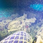 En una bodega oscura del Thistlegorm, una moto volcada detrás de un neumático de camión, iluminada con linterna