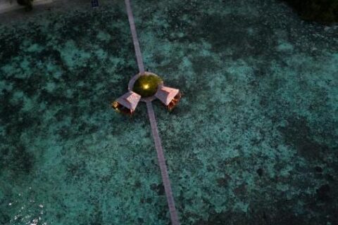 Vista aérea nocturna de un largo muelle de madera que sale de la playa, con dos cabañas sobre pilotes a mitad de camino