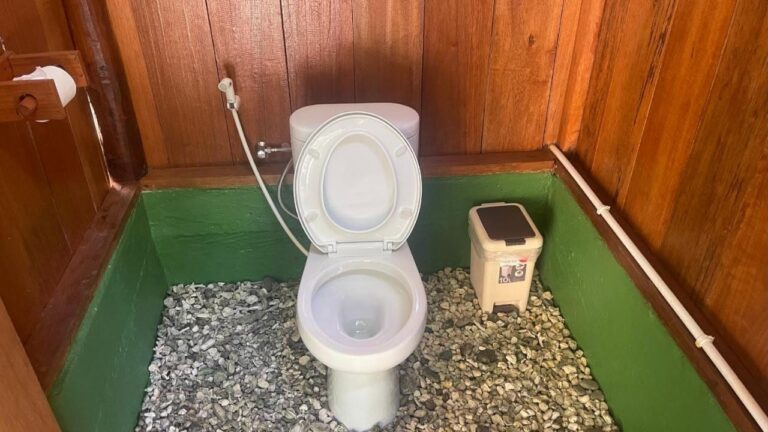 Un inodoro entre paredes de madera, con suelo de guijarros