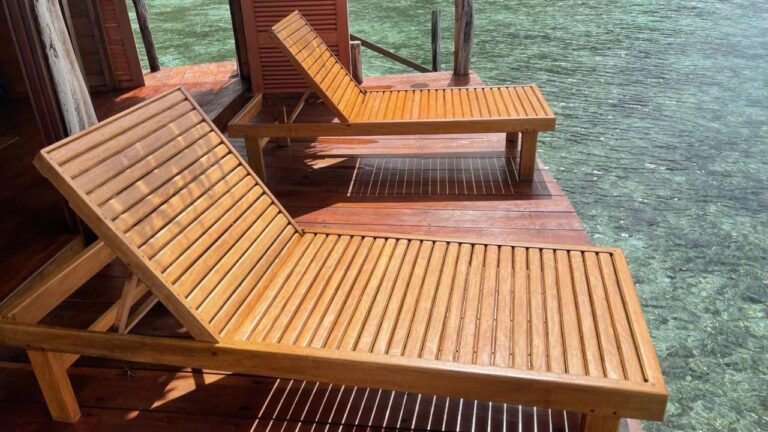Dos tumbonas de madera en la terraza de un bungalow, sobre el agua clara
