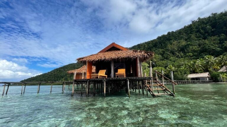 Un bungalow del Nyande Raja Ampat sobre pilotes, encima del agua clara, al pie de una colina boscosa