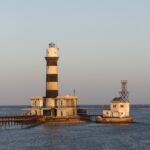 El faro de Daedalus, una torre de franjas blancas y negras sobre el arrecife, con sus edificios y su muelle metálico, al atardecer