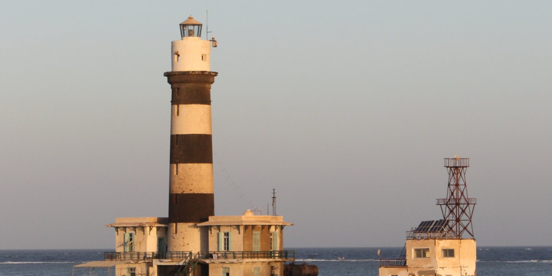 El faro de Daedalus, una torre de franjas blancas y negras sobre el arrecife, con sus edificios y su muelle metálico, al atardecer