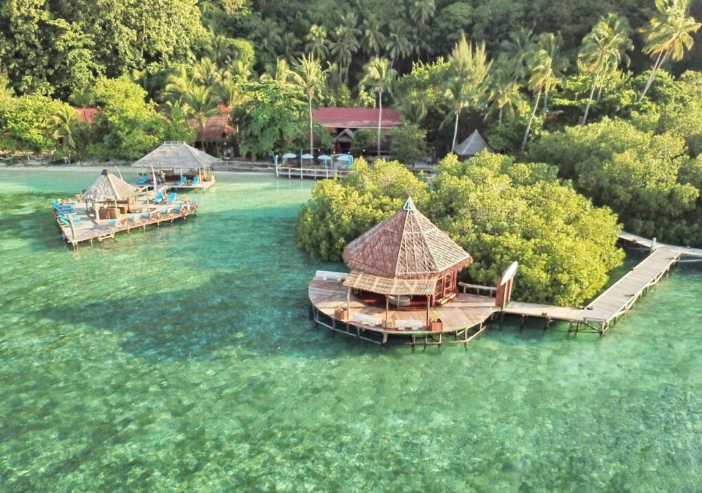 Vista aérea del Raja Ampat Dive Lodge, con sus pontones sobre pilotes y sus tejados rojos bajo las palmeras