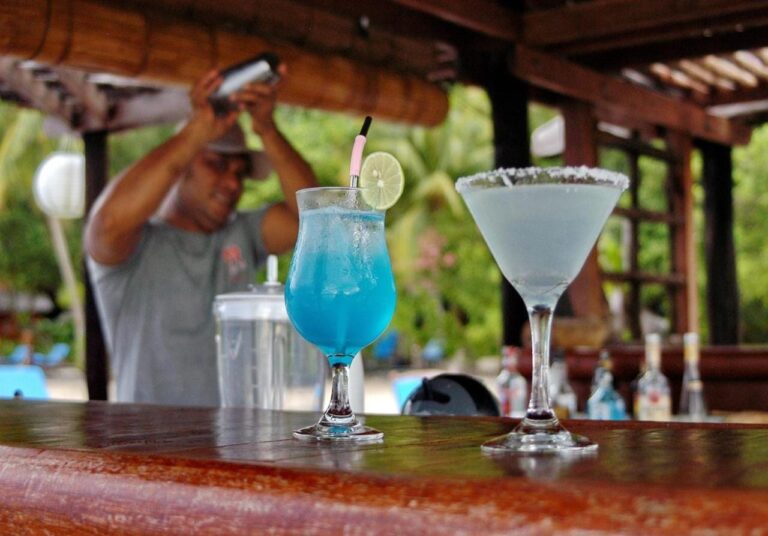 Dos cócteles, uno de ellos azul, sobre la barra de madera del bar, delante del barman