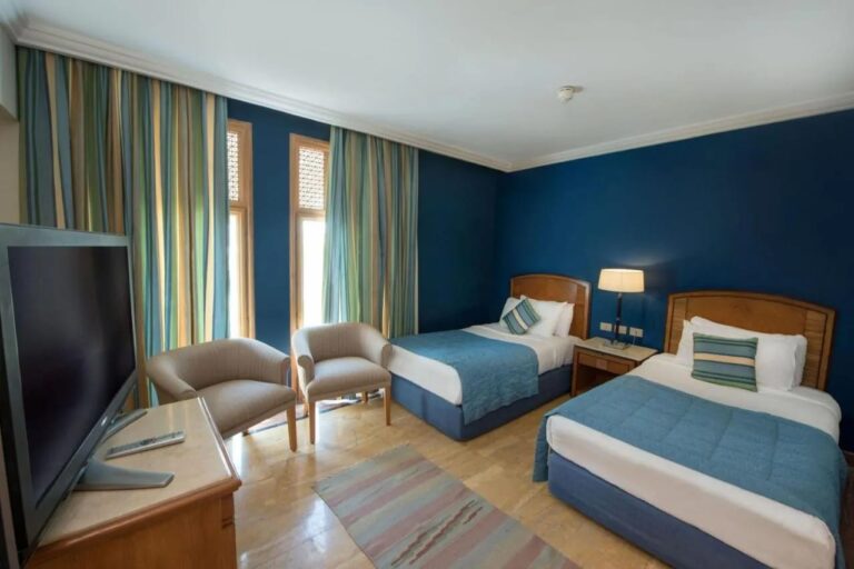 Una habitación con dos camas y paredes azules, con dos sillones frente a las ventanas