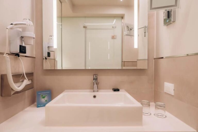 Un lavabo blanco bajo un espejo iluminado, con un secador de pelo en la pared