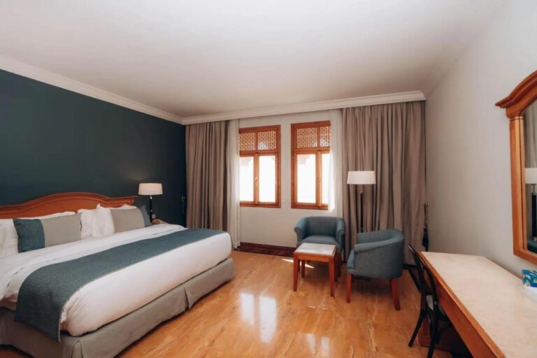 Una habitación con cama grande, una pared verde oscuro y dos sillones azules