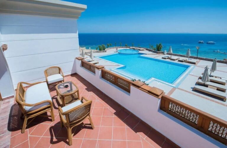 Una terraza con muebles de ratán sobre una gran piscina y el mar Rojo, en el Reef Oasis Beach Resort