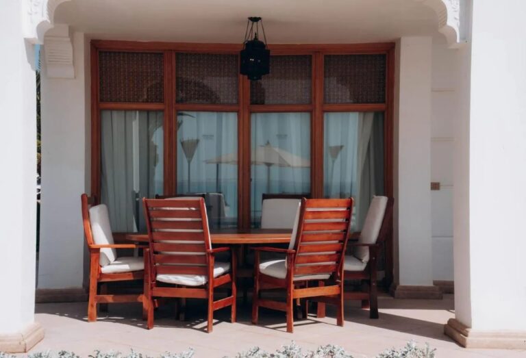 Una terraza cubierta con una mesa de madera y seis sillas, bajo un farol