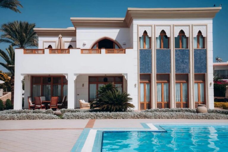 Un edificio blanco del Reef Oasis Beach Resort, con ventanas en arco y paneles de mosaico azul, frente a una piscina
