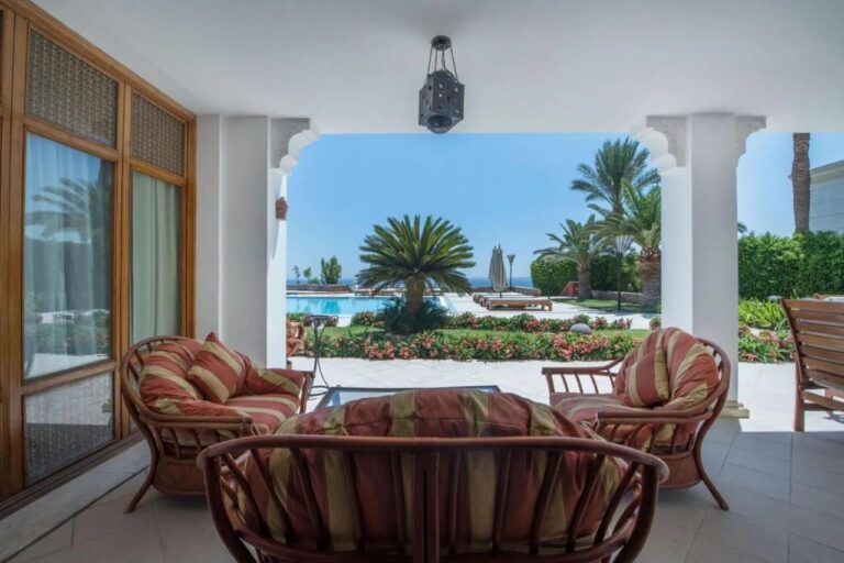 Una terraza cubierta con muebles de ratán, frente al jardín florido, a una piscina y al mar