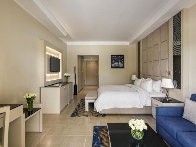 Una habitación con cama grande, un sofá azul y flores blancas sobre la mesa