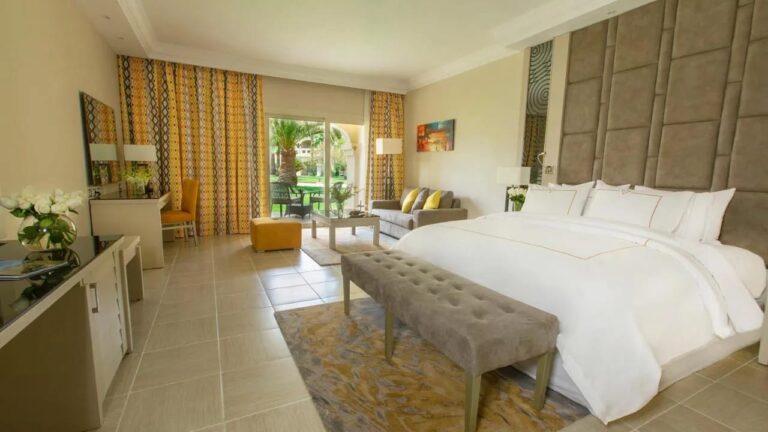 Una habitación con cama grande abierta al jardín, con un banco a los pies de la cama