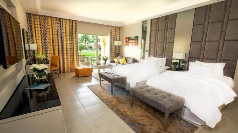 Una habitación con dos camas abierta al jardín, con bancos a los pies de las camas
