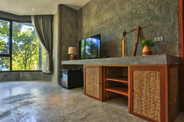 Una televisión sobre un mueble de madera y ratán, junto a un minibar y un ventanal