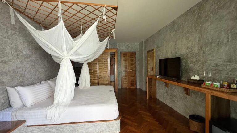 Una habitación con parqué en espiga, una cama con mosquitero, una televisión y un rincón para el té