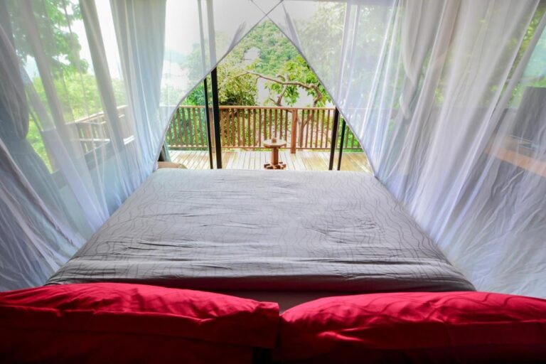 Vista desde la cama, a través del mosquitero, de una terraza de madera y los árboles