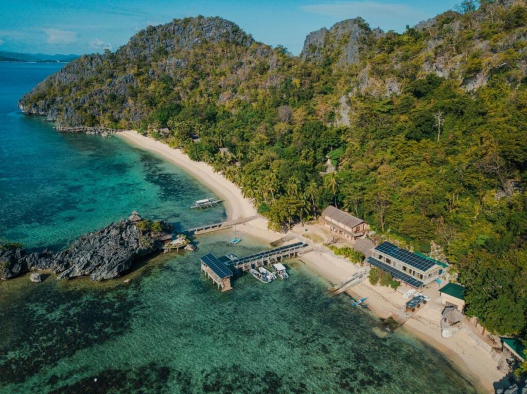 Vista aérea del Sangat Island Dive Resort, con su playa, su embarcadero y sus barcos, al pie de los acantilados