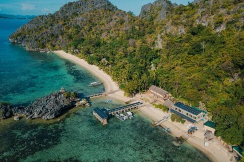 Vista aérea del Sangat Island Dive Resort, con su playa, su embarcadero y sus barcos, al pie de los acantilados