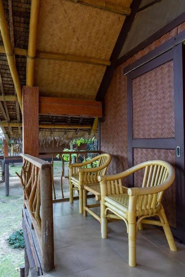 Una veranda embaldosada con dos sillones de ratán, junto a una pared trenzada