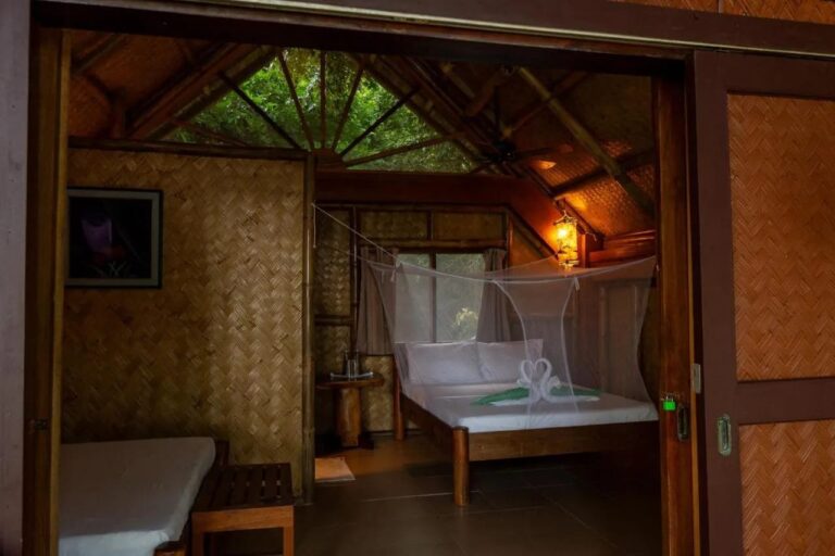 Una habitación con paredes de bambú trenzado, una cama doble con mosquitero y una cama individual