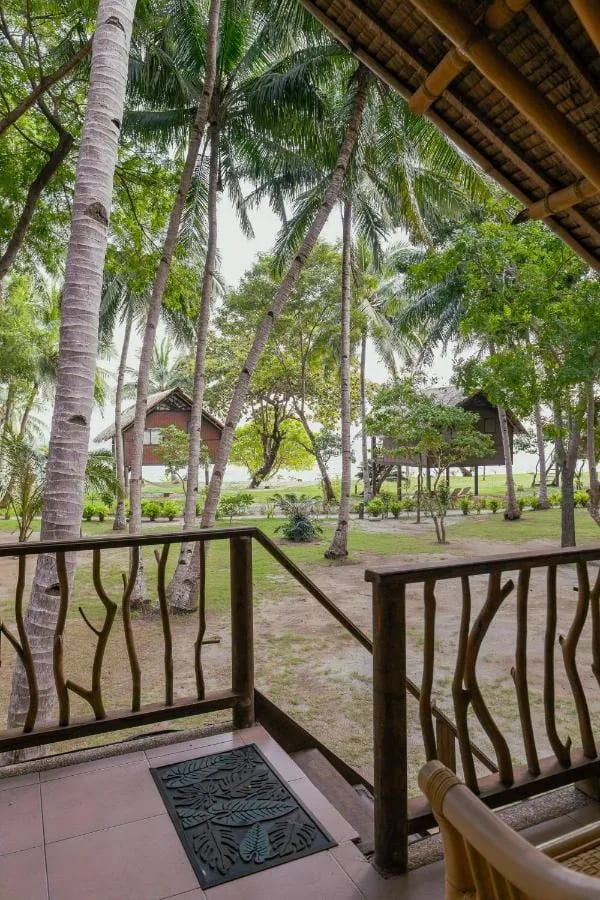 La vista desde una veranda de las palmeras, el césped y unos bungalows sobre pilotes