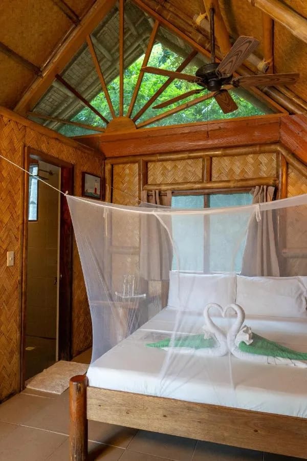 Una cama con mosquitero con dos cisnes hechos con toallas y, al fondo, el baño