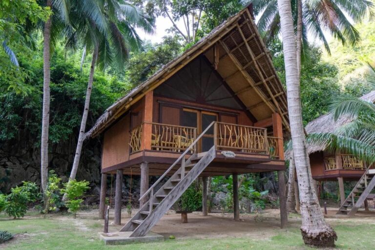 Un bungalow sobre pilotes del Sangat Island Dive Resort, con una escalera de madera, bajo las palmeras