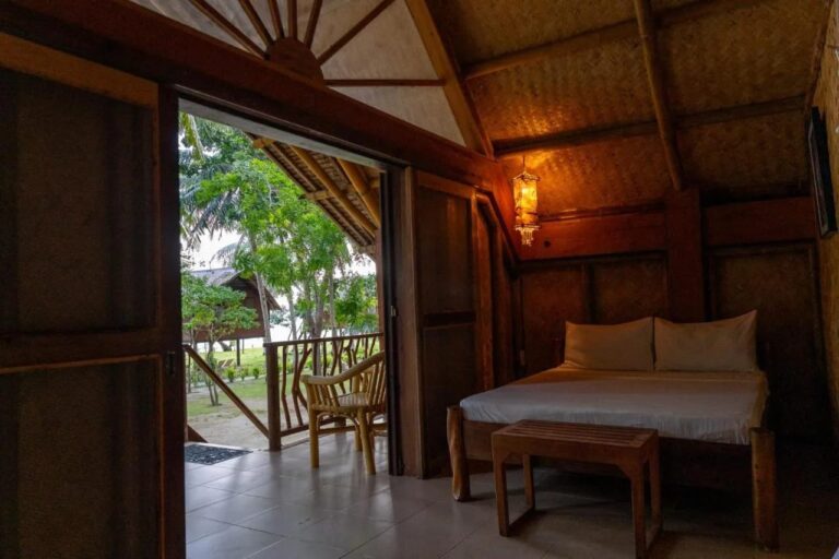 Una habitación con cama doble abierta a la veranda, con un sillón de ratán y el jardín