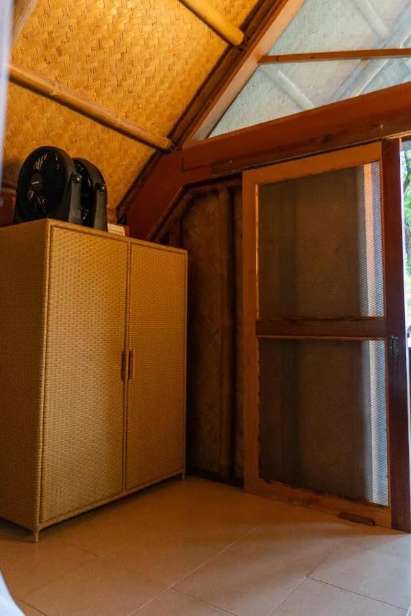 Un armario trenzado con dos ventiladores encima, junto a una puerta mosquitera