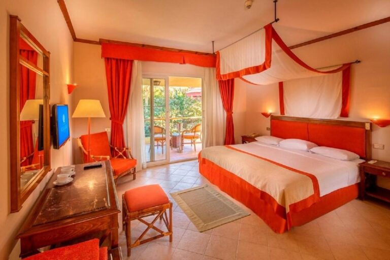 Una habitación con cama grande bajo un dosel blanco y naranja, abierta a un balcón