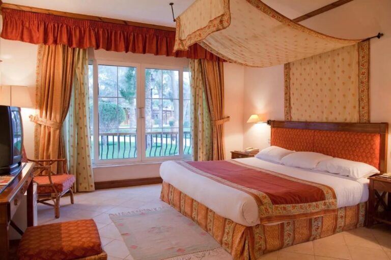 Una habitación con cama grande bajo un dosel de flores, con un ventanal que da al jardín
