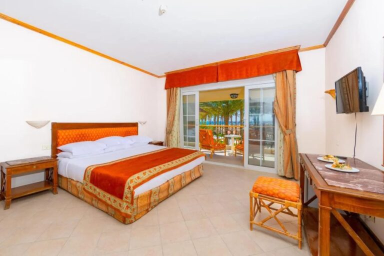 Una habitación con cama grande abierta a un balcón, con las palmeras y el mar al fondo