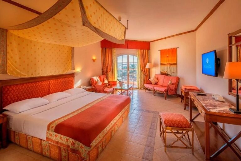 Una habitación amplia con una cama bajo un dosel, un sofá naranja y un escritorio