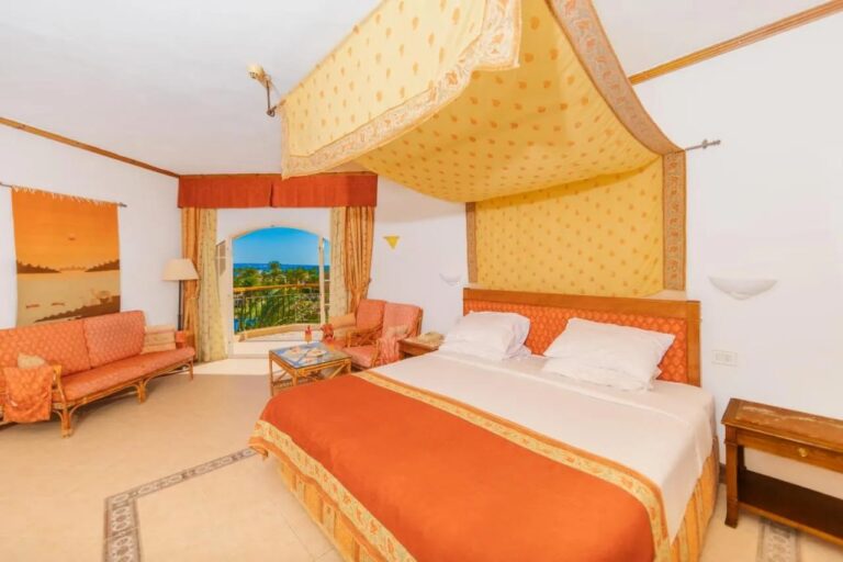 Una habitación del Siva Grand Beach con una cama grande bajo un dosel amarillo, un salón naranja y el mar a lo lejos